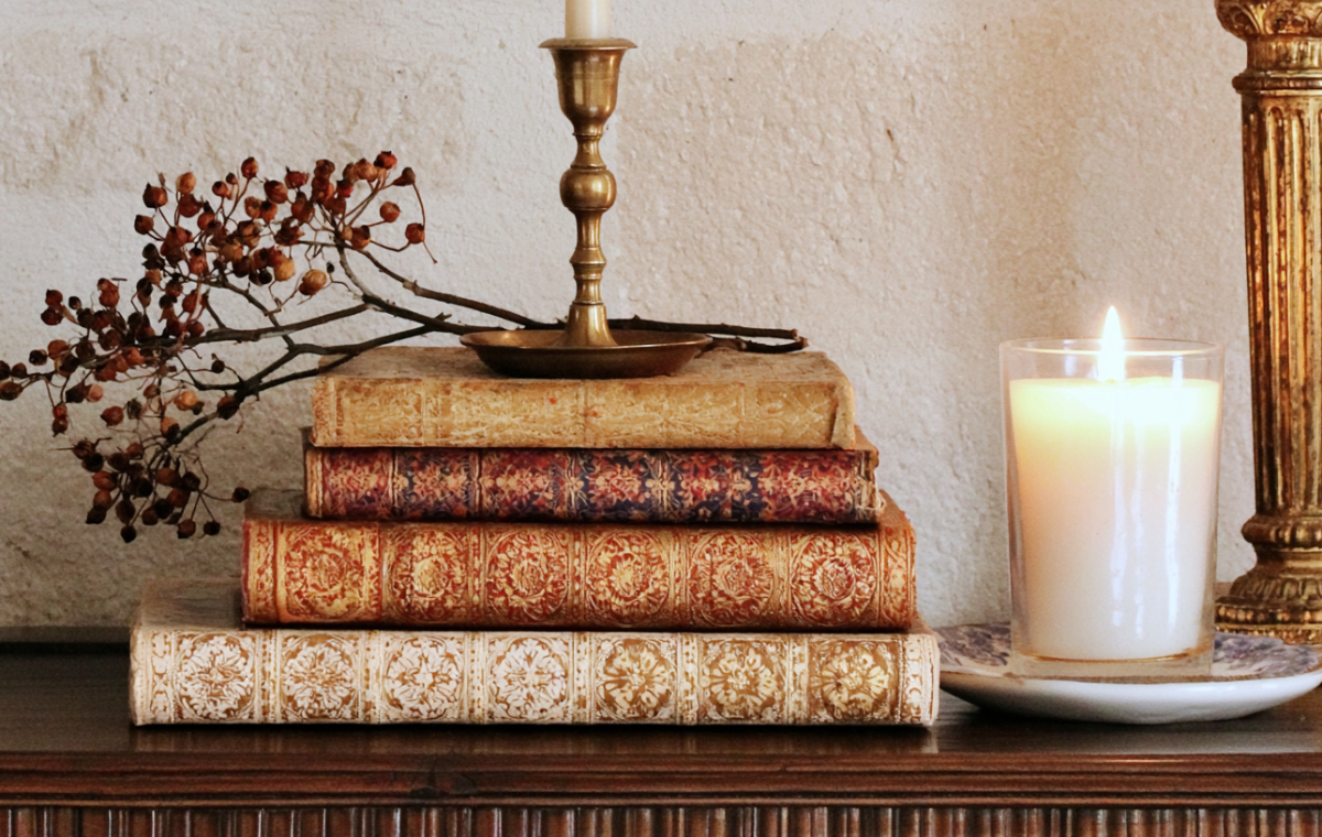 Vintage book stack decor styled with a brass candlestick and glowing candle on a wooden console