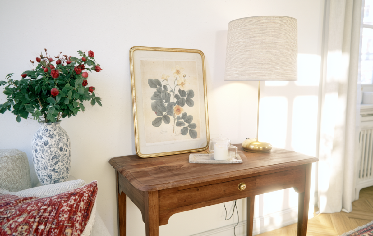 Vintage console table styling with botanical art, a brass lamp, and a vase of red roses in a bright living room.