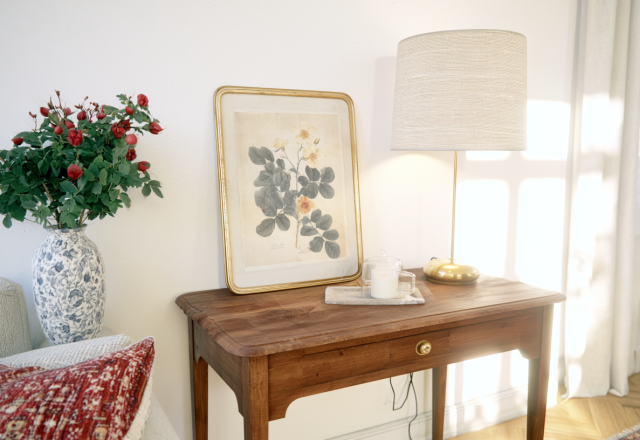 Vintage console table styling with botanical art, a brass lamp, and a vase of red roses in a bright living room.