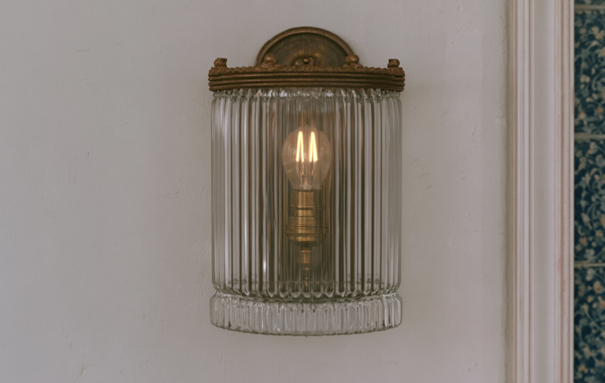 A vintage glass wall sconce with a ribbed shade and warm filament bulb mounted on a textured white wall.