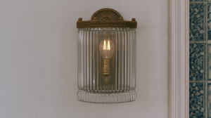 A vintage glass wall sconce with a ribbed shade and warm filament bulb mounted on a textured white wall.