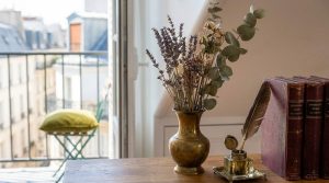 Vintage home office styling featuring brass vase with dried lavender, inkwell with quill, and antique books next to a balcony window.