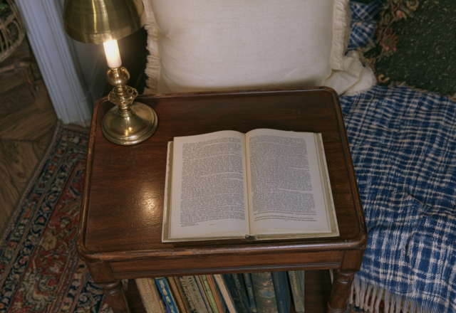 Vintage reading nook featuring an open book, brass lamp, and blue plaid blanket on a wooden side table