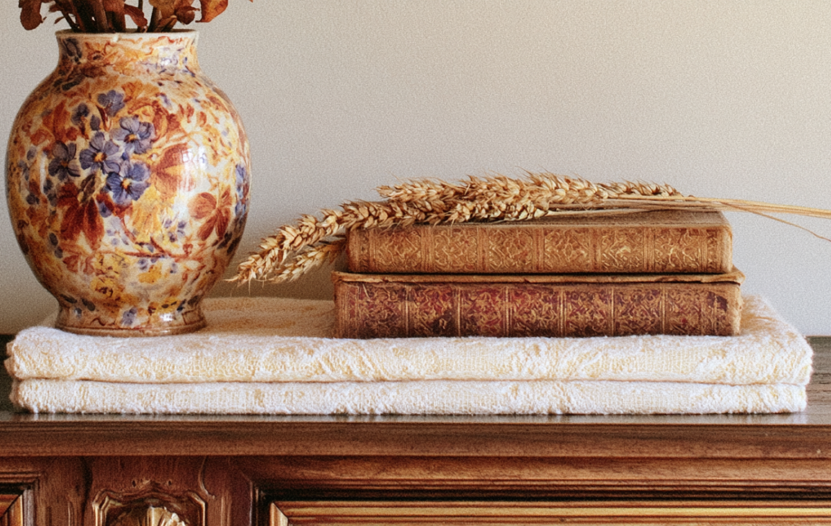 Vintage shelf styling featuring antique books, a floral ceramic vase, and dried wheat on a wooden console.