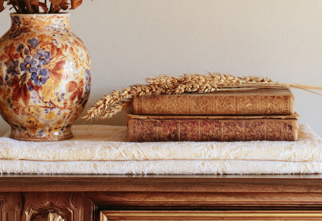 Vintage shelf styling featuring antique books, a floral ceramic vase, and dried wheat on a wooden console.