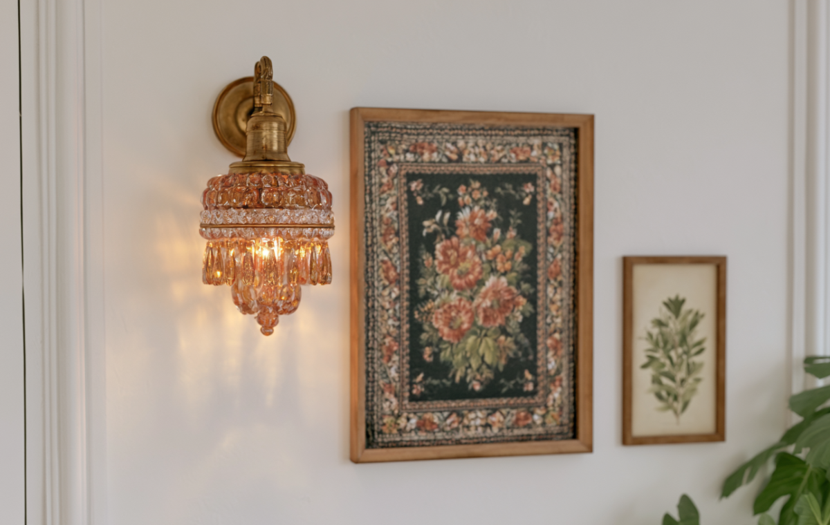 Vintage brass wall sconce with amber crystal glass paired with framed botanical art in a hallway.