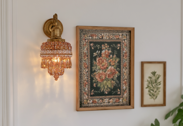 Vintage brass wall sconce with amber crystal glass paired with framed botanical art in a hallway.