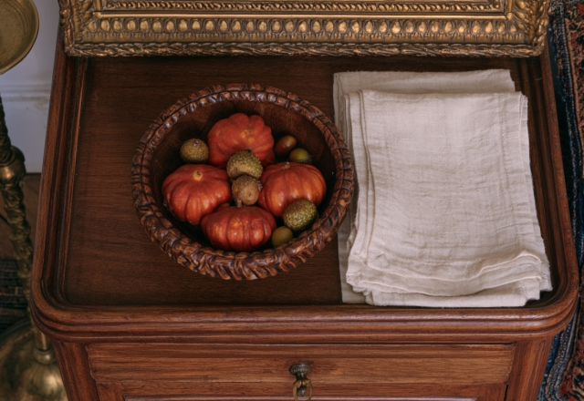 Close-up of a vintage wooden nightstand styled with a wooden bowl of mini pumpkins and linen napkins.