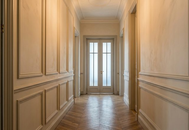 Elegant wainscoting hallway design with neutral wall panels and chevron hardwood flooring.