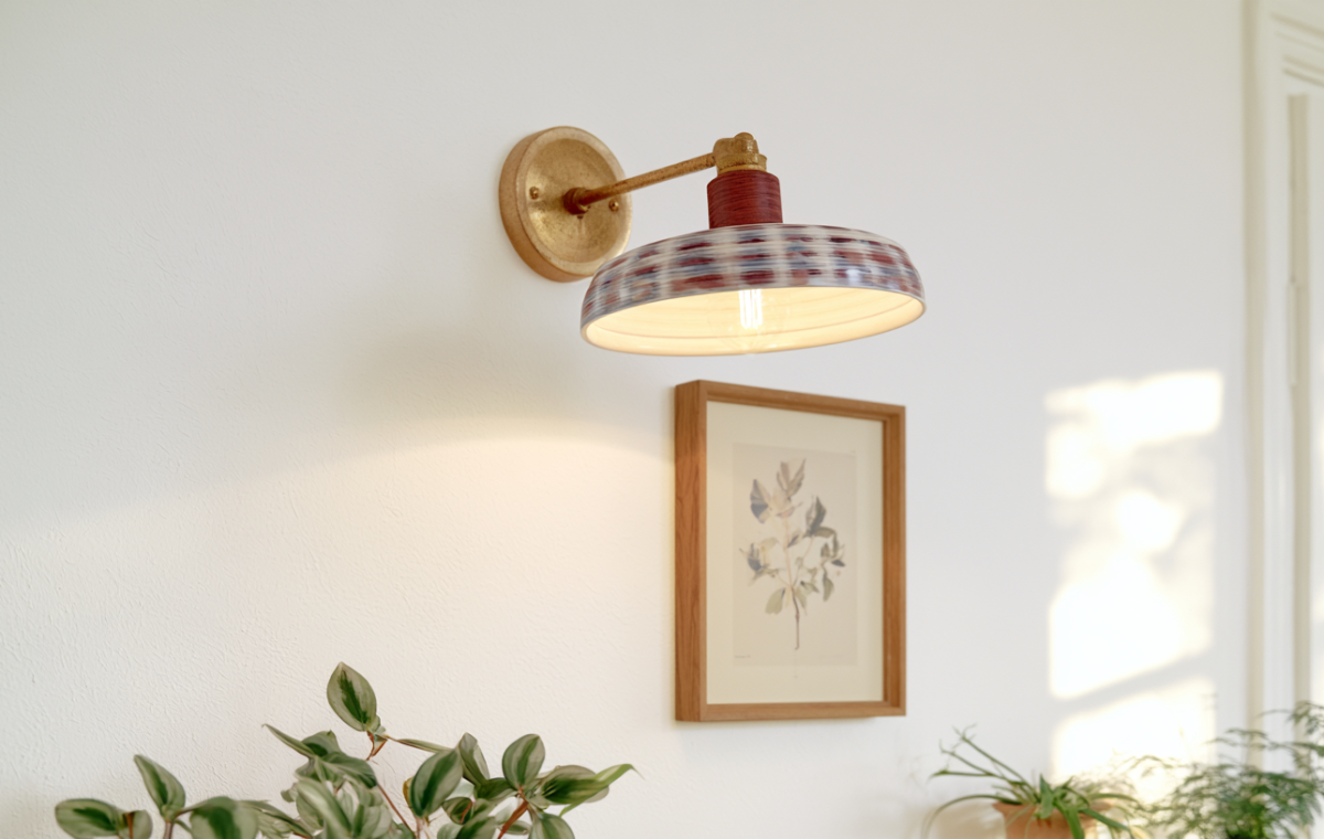 A decorative patterned wall sconce lighting fixture mounted above framed botanical art and green plants.