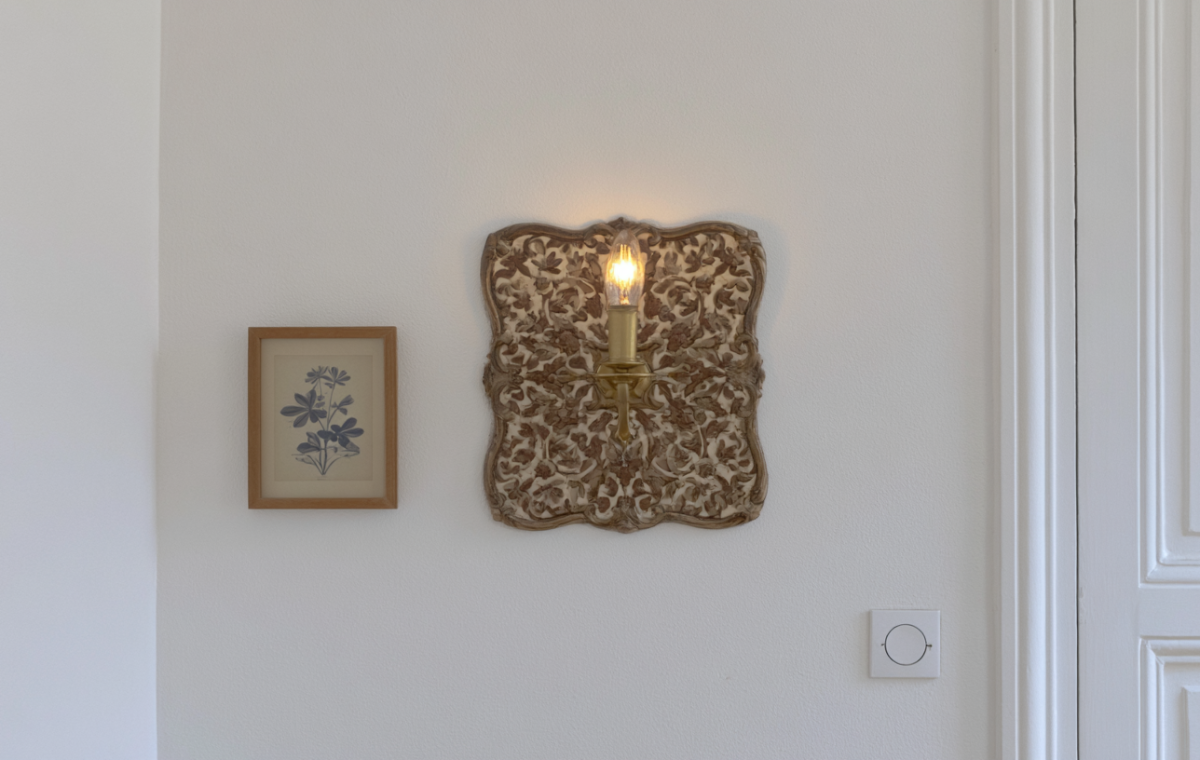 Vintage brass wall sconce lighting fixture mounted next to a framed botanical print on a white wall