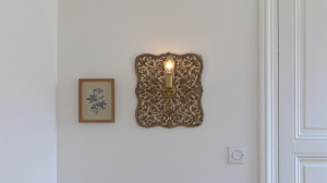 Vintage brass wall sconce lighting fixture mounted next to a framed botanical print on a white wall