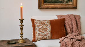 Warm interior styling featuring a brass candle holder, textured pillow, and cozy throw blanket on a sofa.