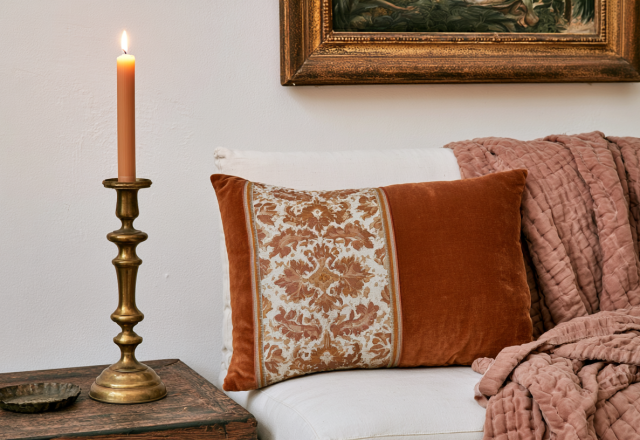 Warm interior styling featuring a brass candle holder, textured pillow, and cozy throw blanket on a sofa.