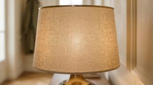 A close-up of a textured linen lampshade with a warm internal glow on a brass base.