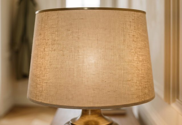 A close-up of a textured linen lampshade with a warm internal glow on a brass base.