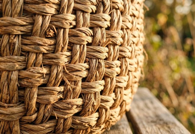 Close up of a natural fiber storage basket resting on a weathered wooden table in warm light