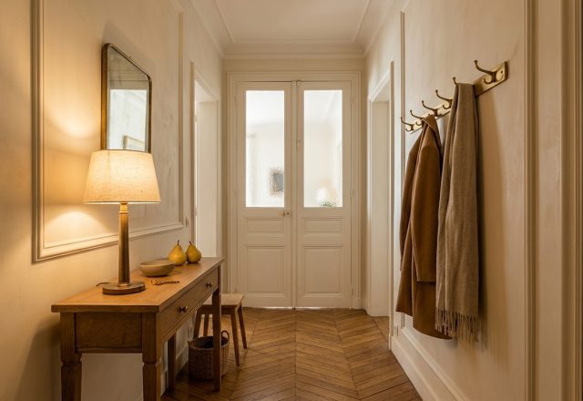 A warm hallway featuring timeless entryway design with chevron wood floors and brass hardware.