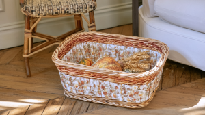 A fabric-lined wicker storage basket filled with harvest accents sitting on a wood floor.