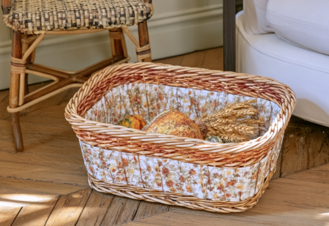 A fabric-lined wicker storage basket filled with harvest accents sitting on a wood floor.