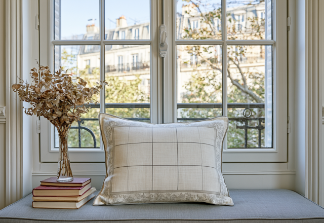 Cozy window seat decor featuring a neutral grid pillow, dried botanicals in a glass vase, and vintage books.