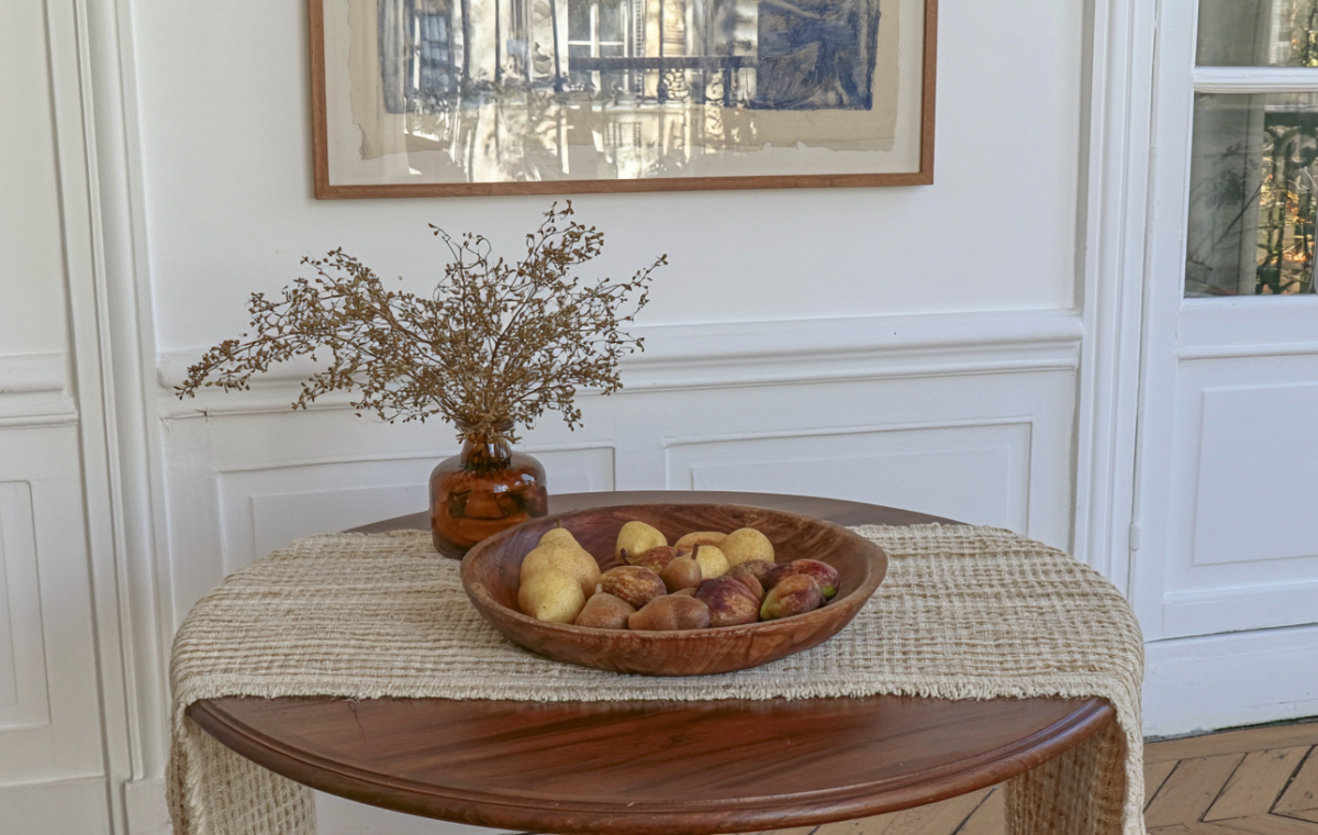 Wooden dining table decor featuring a neutral linen runner and a wooden bowl filled with pears and figs.