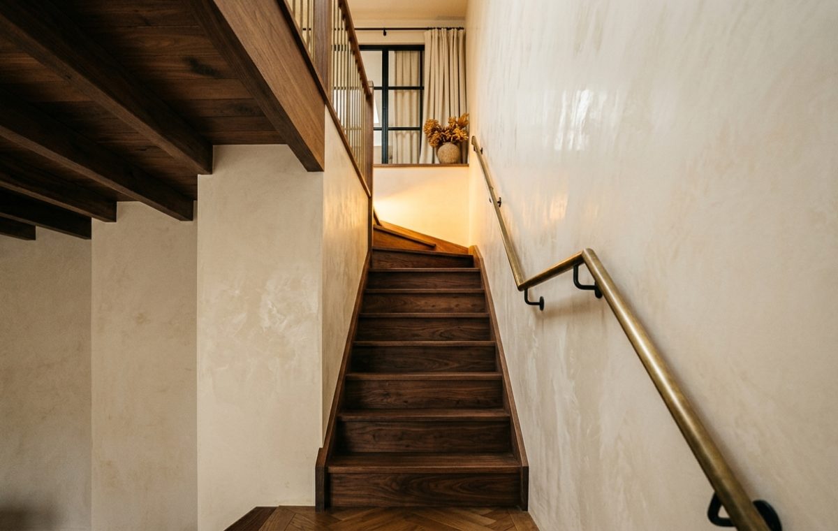 Modern wooden staircase design with textured plaster walls and a brass handrail