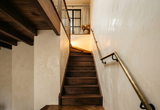 Modern wooden staircase design with textured plaster walls and a brass handrail